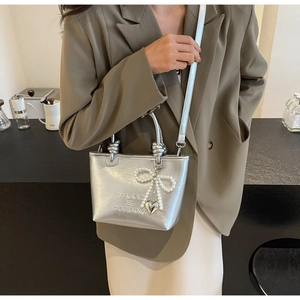 Détail du sac argenté miroir avec charm nœud en perles et pendentif en forme de cœur
