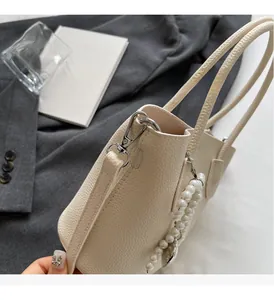 Detail of cream leather bucket bag with pearl charms and silver hardware on a blazer