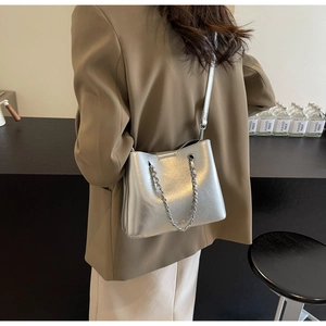 Detail of silver metallic handbag with chain strap worn by model against a minimal backdrop
