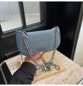 Detail of light blue denim shoulder bag featuring silver metal studs and a chain strap