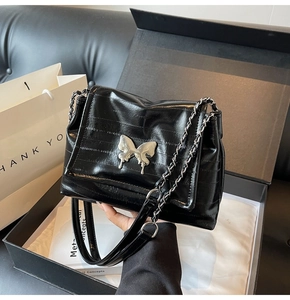 Detail of black embossed leather shoulder bag featuring a silver butterfly clasp in a gift box
