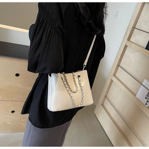Detail view of white glossy bucket bag with silver chain strap worn over the shoulder