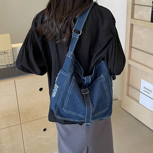 Deep blue denim crossbody bag with white stitching and frayed edges shown on model