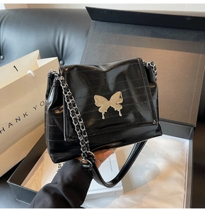 Detail of black glossy leather bag with silver butterfly buckle and chain strap