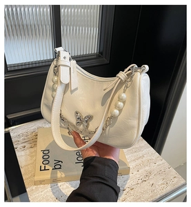 Detail of white leather underarm bag with silver butterfly charm and pearl chain