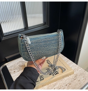 Detail of light blue denim underarm bag featuring silver rivets and chunky metal chain