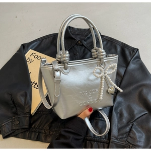 Détail du sac seau argenté avec poignée nouée, nœud perlé et breloque cœur sur cuir