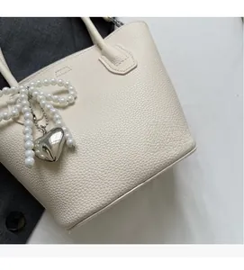 Macro shot of off-white lychee texture leather handbag with pearl bow and silver heart pendant
