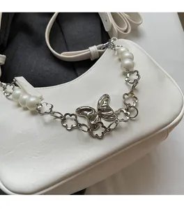 Detail view of a white leather underarm bag featuring a metallic butterfly and pearl chain