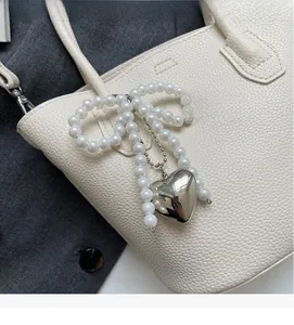 Close-up of pearl bow bag charm with a silver heart pendant on white leather purse