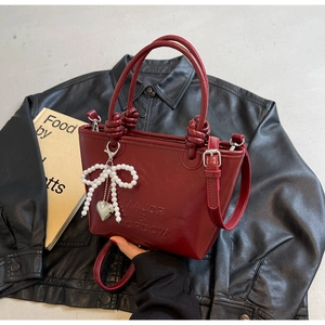 Détail du sac seau bordeaux en cuir brillant avec poignée nouée et breloque perle