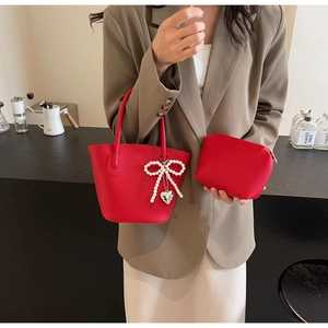 Detail of red lychee textured tote bag with pearl bow and heart metal pendant