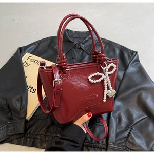 Détail du sac seau en cuir verni rouge foncé avec nœud en perles et poignée nouée