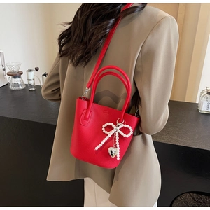 Detail of red bucket bag with litchi texture, pearl bow charm and heart pendant