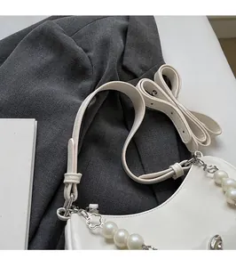 Detail of white leather shoulder bag with decorative pearl chain and clover pendant