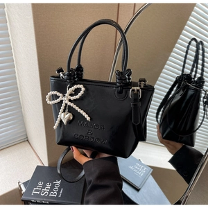 Détail du sac seau noir brillant avec nœud en perles et pendentif en forme de cœur argenté