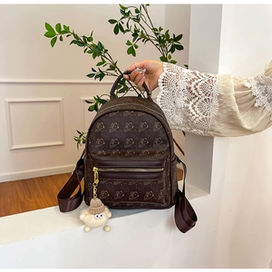 Detail of brown faux leather backpack with bear print and soft beige pom-pom pendant