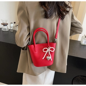 Red lychee pattern bucket bag with pearl bow and heart charm worn by a model
