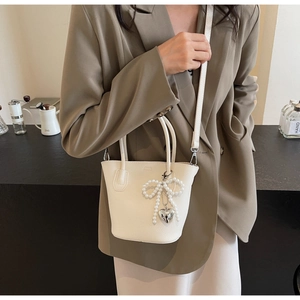Detail of cream bucket bag with pearl bow and silver heart charm on litchi leather