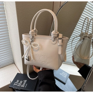 Détail du sac cabas en cuir crème avec pendentif perle et logo embossé de haute qualité