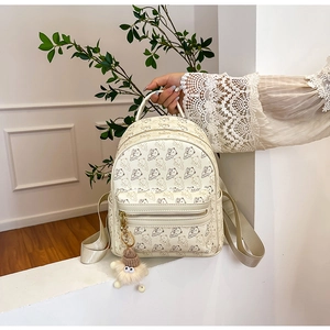 Close-up of beige mini backpack featuring cartoon bear print and a cute fur pompom charm
