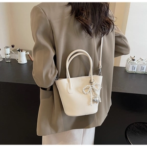 Close-up of a white bucket bag with lychee texture and pearl bow charm on a model