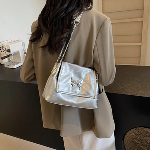 Silver metallic tote bag with butterfly buckle and chain strap shown on model shoulder