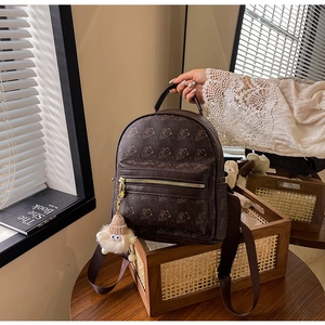 Detail of a brown mini backpack with golden bear patterns and a plush bear charm