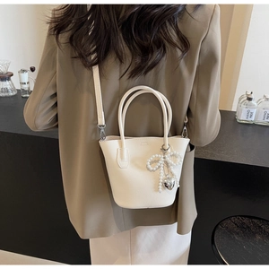 Detail view of cream bucket bag with lychee texture and pearl bow charm accessory
