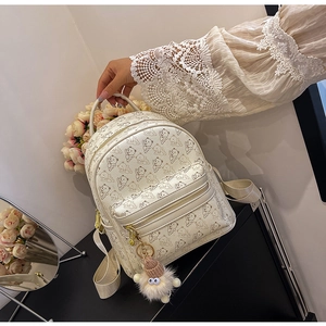 Close-up of cream mini backpack with cartoon bear patterns and plush charm detail