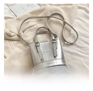 Detail of silver bucket bag with embossed texture and metal buckle straps on bed