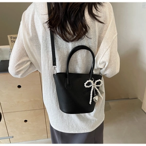 Detail view of black lychee leather bucket bag with pearl bow and heart pendant