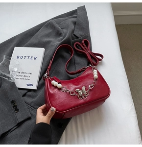 Detail of dark red crescent bag featuring pearly butterfly chain and glossy finish