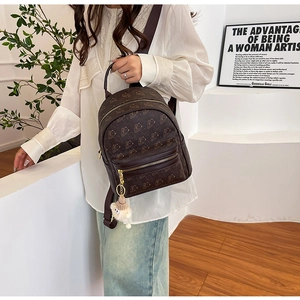 Detail view of mini brown backpack with bear print and plush ball pendant on a model