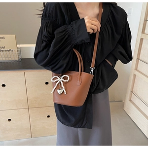 Close-up of brown bucket bag with pearl bow and silver heart pendant detail