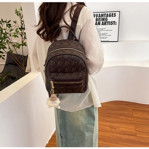 Mini brown backpack with pattern print, gold zippers and plush pendant detail on a model