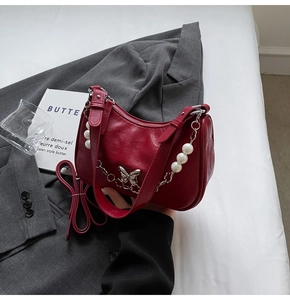 Detail of burgundy half-moon shoulder bag with silver butterfly clasp and pearl chain