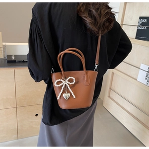 Detail of brown litchi leather bucket bag featuring pearl bow and silver heart charm