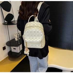 Detail of cream backpack with brown bear prints and plush ball charm in a modern room