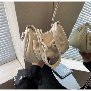 Close-up of cream bow shoulder bag featuring a metallic zipper and soft faux leather texture