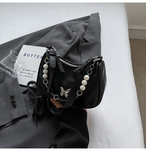Detail of black underarm bag featuring silver butterfly and pearl chain strap