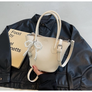Close-up of cream lychee leather bucket bag featuring a large pearl bow and heart charm