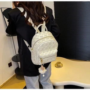 Detail view of white leather backpack featuring cartoon patterns and plush charm on the model