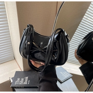 Detail of black glossy faux leather shoulder bag featuring a large bow and zipper