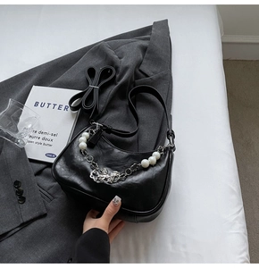 Detail of black hobo bag with pearl chain and butterfly pendant on grey blazer