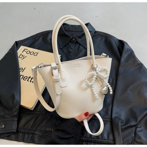 Close-up of white pebbled leather bucket bag with pearl bow and silver heart charm