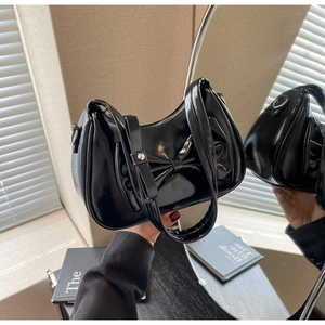 Close-up of black glossy shoulder bag featuring a large bow detail and a wide handle