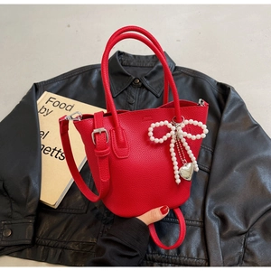 Detail of red lychee grain handbag featuring pearl bow charm and silver heart pendant