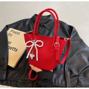 Detail of red pebbled leather bucket bag with white pearl bow and silver heart pendant
