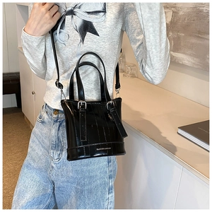 Detail of a glossy black bucket bag with adjustable strap worn by a model